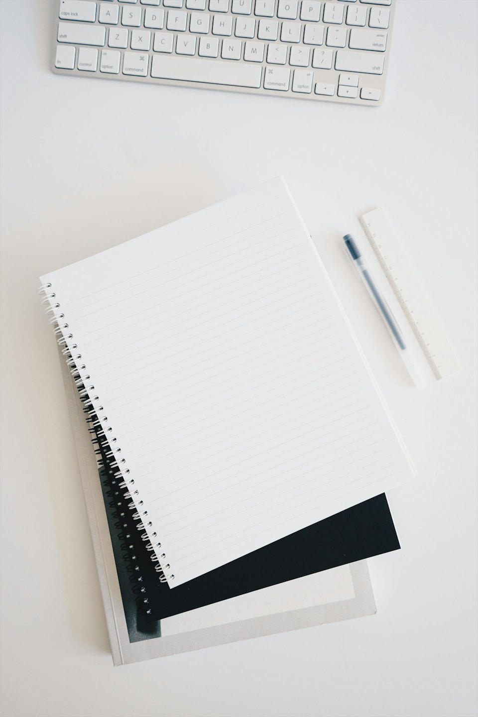 Minimalistischer Arbeitsplatz mit Notizbüchern, Stift, Lineal und Tastatur.